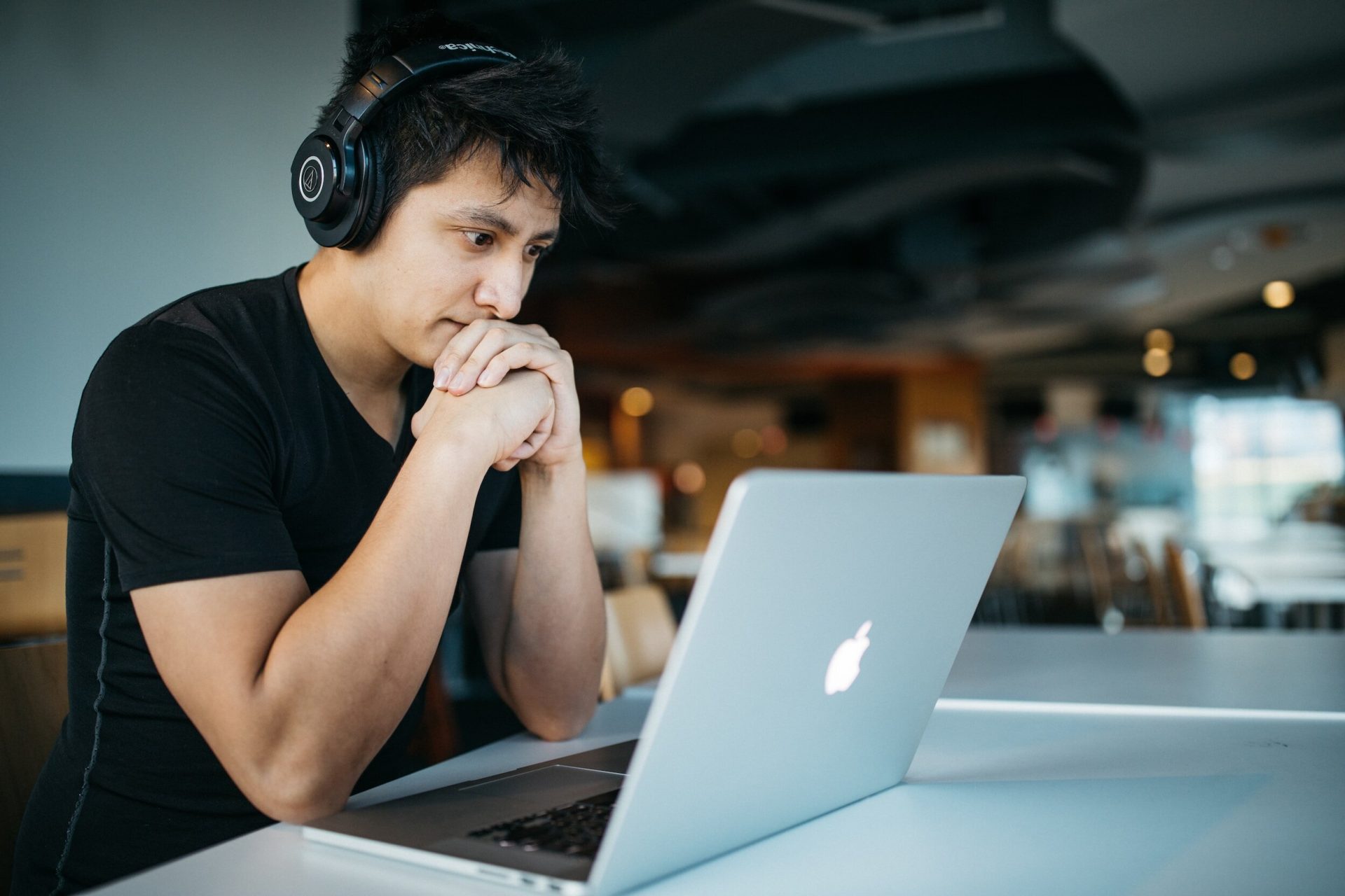 A man with headphones sits at a table, focused on his laptop while working or studying.